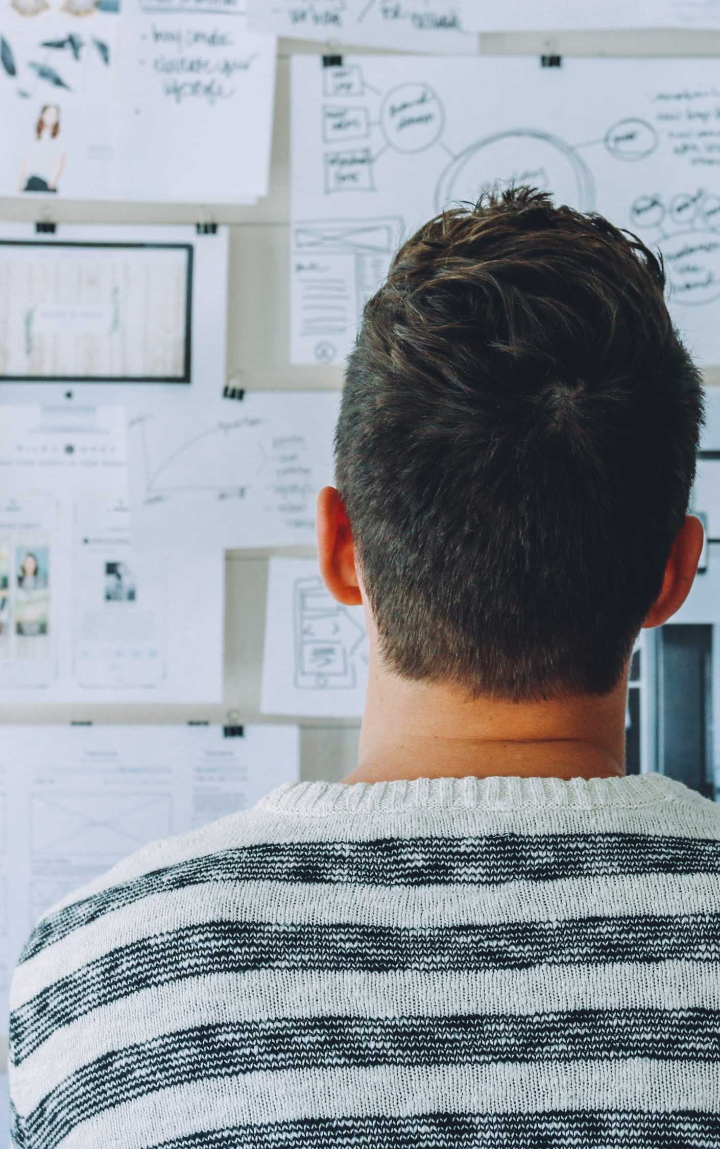 man looking at papers and graphics on a pin board